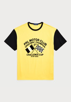 T-shirt de algodão amarelo com mangas curtas pretas. Apresenta texto gráfico e bandeiras de corrida impressas em preto. Gola redonda.