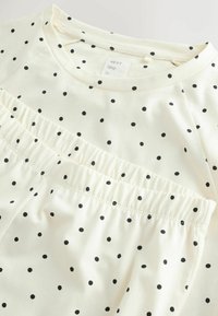 Kremfarvet T-shirt med sorte polkaprikker, udstyret med en rynket talje og rund halsudskæring. Blødt bomuldsstof.
