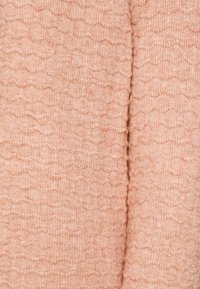 Persikofärgad texturerad tyg med ett vågmönster. Mjukt, stickat material med en något ludden yta. Lämpligt för kläder eller möbelklädsel.