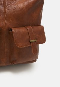 Brown leather backpack with a textured finish, featuring a front pocket secured by a strap and brass-colored hardware.