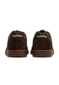 Sneaker in suede marrone con una finitura testurizzata, dotate di un tallone nero e un logo dorato stampato. Suola in gomma con un design a profilo basso.