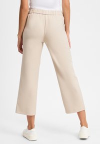 Beige weit geschnittene Hosen mit einem elastischen Bund, aus einem weichen Stoff gefertigt, mit einer glatten Textur und einem lässigen Design.