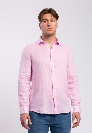 Camicia di lino rosa chiaro con maniche lunghe, colletto, chiusura con bottoni e finitura leggermente strutturata. Indossata con jeans blu.