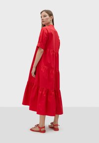 Robe rouge à volants en tissu léger, avec des manches courtes et un col rond. Portée avec des sandales plates rouges.