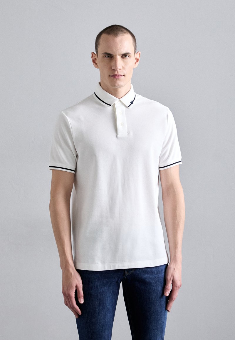 White polo shirt in cotton with a two-button placket, black accents on the collar and sleeves, paired with dark blue jeans.