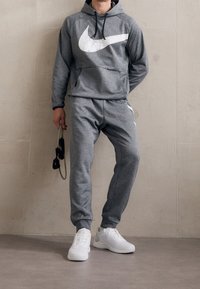 Sweat à capuche gris avec un logo Nike blanc, accompagné d'un pantalon de survêtement gris assorti. Comprend une poche kangourou et des chaussures de sport blanches.