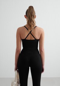 Musta kuntoiluasu, johon kuuluu istuva crop-top, jossa on ristikkäiset hihnat, ja korkeavyötäröiset legginsit, jotka on valmistettu tekstuurista joustavaa materiaalia.