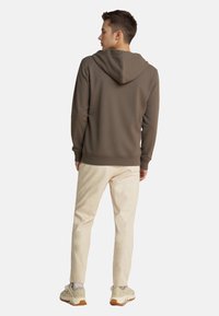 Sudadera marrón con un acabado texturizado, bolsillo canguro y capucha ajustable, combinada con pantalones beige claros y zapatillas claras.