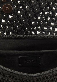 Borsa nera intrecciata con aperture testurizzate, dotata di una fodera in tessuto e di un'etichetta in pelle con un marchio. I dettagli includono una chiusura a bottone.