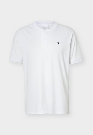 Fehér rövid ujjú galléros póló két gombbal és egy kis fekete logóval a bal mellrészen, egyszínű háttér előtt.