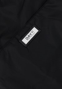 Etichetta in tessuto nera con "DAY ET" e "BIRGER MIKKELSEN" in bianco, cucita su un materiale nero testurizzato, evidenziando il logo del marchio.