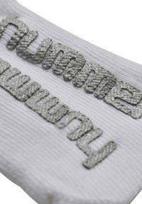 Hvidt tekstilpatch med hævet grå skrift og en struktureret overflade. Designet inkluderer et tydeligt mønster og præget stil.