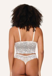 Hvid blonde bralette og matchende strings, indviklet blomster mønster, blød tekstur, justerbare stropper, bølgede kanter, afslørende rygdesign.