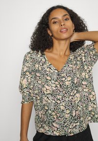 Blusa floral com fundo preto, featuring flores em pastéis de rosa, amarelo e verde, e mangas curtas bufantes. Design em V.