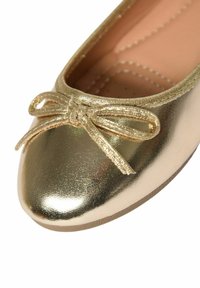 Ballerine dorata e lucida con punta arrotondata, caratterizzata da un piccolo fiocco sulla parte frontale e una superficie sintetica liscia.