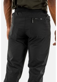 Schwarze Sporthose mit lockerer Passform, elastischem Taillenbund und einem Reißverschlussfach auf der Rückseite. Sie hat einen glatten, leichten Stoff mit dezentem Glanz.