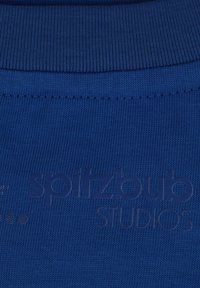 Blauer Strickstoff mit aufgesticktem "spitzbub STUDIOS"-Logo und sichtbar geripptem Kragenrand.