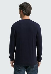 Dunkelblau gestrickter Pullover mit langen Ärmeln und rundem Ausschnitt. Glatte Textur, gerippte Bündchen und Saum, kombiniert mit Jeans.