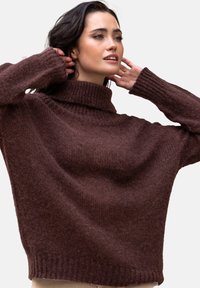 Brązowy, gruby sweter z dzianiny o wysokim, prążkowanym kołnierzu i luźno dopasowanych rękawach, wykonany z miękkiej, teksturowanej przędzy.