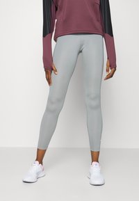 Jasnoszare legginsy wykonane z elastycznego materiału i dopasowanego kroju, w połączeniu z bordową bluzą z długim rękawem z czarnymi akcentami. Białe sneakersy.