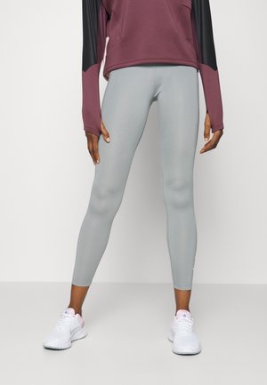 Leggings gris clair en matériau extensible et à design ajusté, associés à un haut à manches longues bordeaux avec des accents noirs. Baskets blanches.