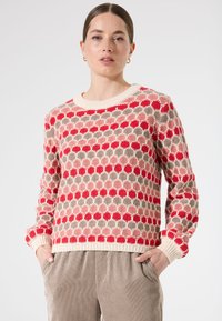 Pull en tricot avec un motif géométrique en rouge, rose, beige et crème. Il a un col rond et des poignets et un ourlet côtelés.