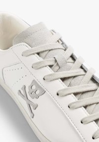 Sneaker in pelle bianca con logo teschio e tibie in suede grigio, linguetta in suede grigio coordinata e lacci bianchi.