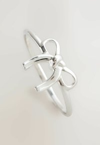 Silver ring features a bow design, polished finish, and a thin band. The bow has smooth curves and distinct loops, creating a delicate look.