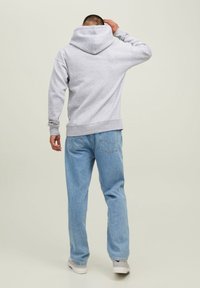 Felpa grigia in cotone con cappuccio ampio, polsini e orlo a costine, abbinata a pantaloni in denim azzurro chiaro e sneaker bianche.