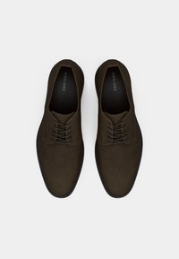 Καφέ δερμάτινα παπούτσια με κορδόνια, στρογγυλεμένη μύτη και μαύρη λαστιχένια σόλα. Το σχέδιο διαθέτει ελάχιστες ραφές και ομαλή υφή.