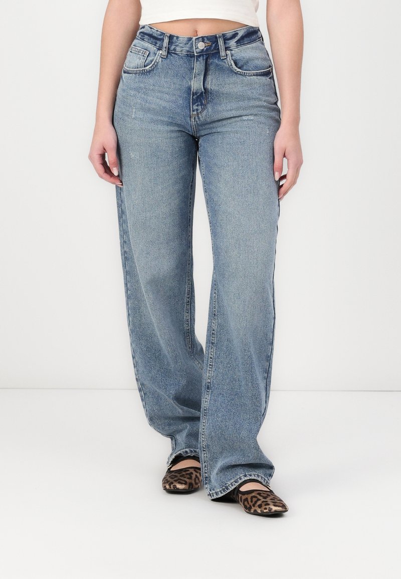 Jean large taille haute bleu clair avec un design classique à cinq poches et un léger délavage. Assorti avec des ballerines à imprimé animal.
