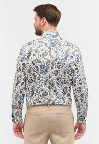 Witte langemouwen blouse met een kleurrijke bloemen- en paisleyprint, met blauwe, groene en gouden accenten. Soepele stof, tailored fit.