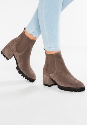 Stivaletti alla caviglia in suede marrone con pannelli elastici laterali, punta tonda e tacco spesso nero. Suola texturizzata per una migliore aderenza. Indossati con jeans skinny azzurri.