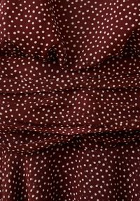 Tissu bordeaux avec des pois blancs, présenté avec une texture froncée et superposée.