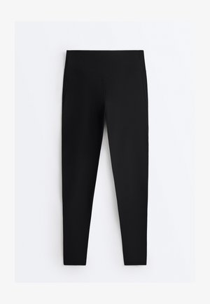 Colanți negri cu talie înaltă, lungime completă, cu un detaliu în formă de V la cusătura taliei, așezați pe o suprafață plată pe un fundal alb.