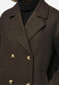 Dubbelknäppt brun ullblandad kappa med en elegant textur, stora slag och glänsande guldfärgade knappar. Har en figursydd silhuett.