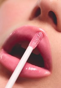 Brillo de labios rosa brillante aplicado con un aplicador blanco sobre labios gruesos, mostrando una textura suave y un brillo sutil.