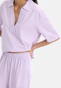 Fioletowy krótki top z kołnierzykiem i haftem kwiatowym na rękawach, w połączeniu z pasującymi spodniami z elastycznym pasem i kieszeniami.