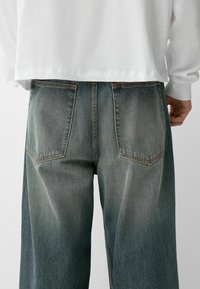 Srajčne jeans hlače širokih nogavic, v bledem modro-sivem odtenku, z zasnovo petih žepov in vidno šivanko vzdolž zadnjih žepov.