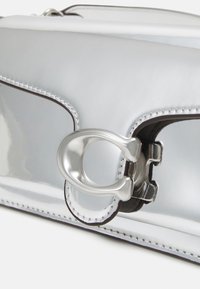 Borsa in pelle verniciata argento con una texture liscia, caratterizzata da una fibbia argentata distintiva e cuciture scure a contrasto lungo i bordi.