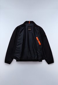 Veste bomber noire ouverte pour montrer la doublure intérieure noire brillante avec languette orange et poche pression sur fond uni clair.