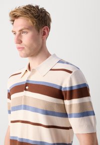 Stripet polo skjorte i beige, brun og blå, med teksturert stoff, krage og knapplukking ved halsen. Korte ermer.