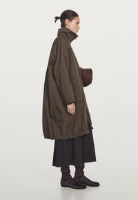 Brązowy oversize'owy płaszcz z wysokim kołnierzem, ściąganym dołem i zapięciem na guziki. Połączony z długą czarną spódnicą i brązowymi, luźnymi botkami do kostki.