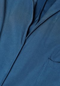 Blaues, glattes Stoffblazer mit einem Reverskragen und einer einzelnen Brusttasche. Weiche Textur und klare Linien schaffen ein maßgeschneidertes Erscheinungsbild.