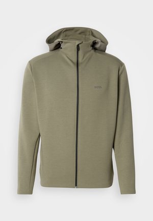 Oliivinvihreä vetoketjullinen huppari, joka on valmistettu sileästä kankaasta. Siinä on korkea kaulus, säädettävä kiristysnyöri huppuosassa sekä hillitty logo rinnassa.