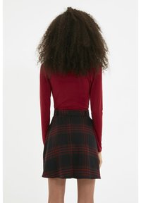 Haut à manches longues rouge et ajusté associé à une jupe mini à carreaux noire et rouge, avec une taille haute et des détails plissés.
