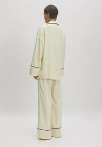 Romige, lichte loungewear set met een lange mouw top en wijde broek, voorzien van zwarte piping details op de manchetten en de zoom.