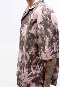 Camicetta a maniche corte con un motivo tie-dye in toni di rosa sfumato e grigio. Presenta una vestibilità rilassata, chiusura con bottoni e tessuto testurizzato.