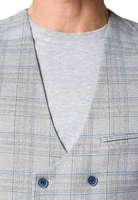 Szary kamizelka w kratę z niebieskim wzorem, dwurzędowy krój i gładki szary t-shirt pod spodem. Teksturowana tkanina i niebieskie guziki.