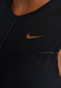 Granatowy sportowy top na ramiączkach z teksturowanej siateczki, złote logo Nike oraz odblaskowe akcenty wzdłuż szwów.